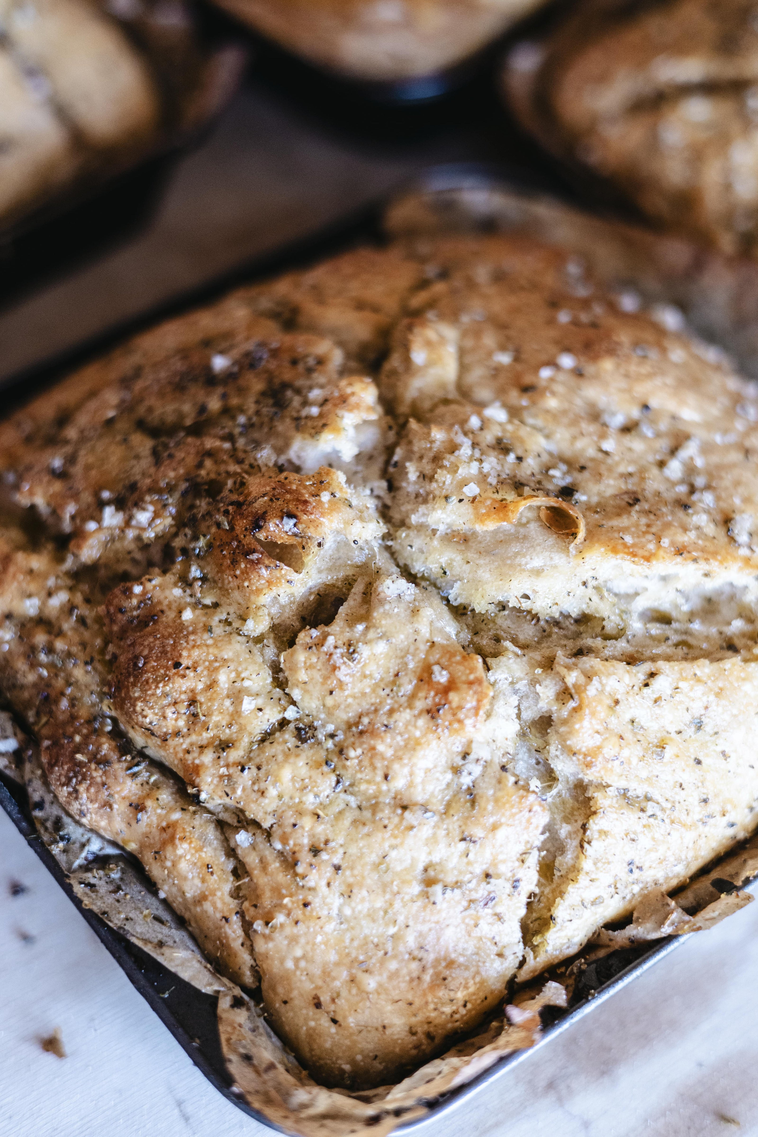 Ką tik iškepta Focaccia duona - jos paviršius padengtas traškia kvepianči žolelių ir druskos plutele.